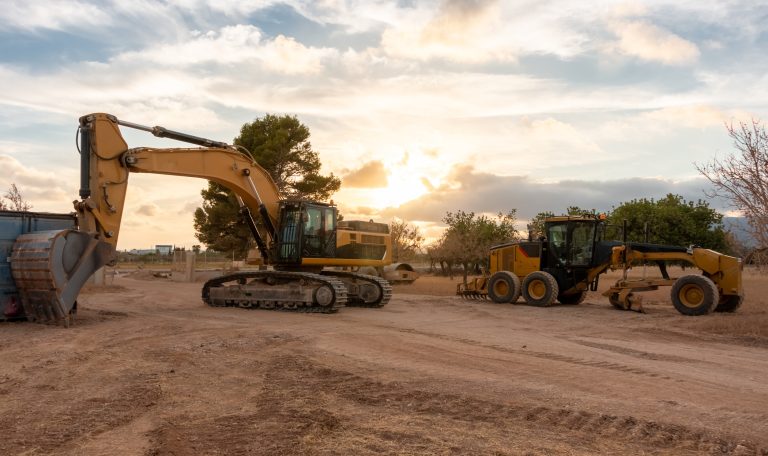 An excavator and a motor grader parked on a construction site at sunset. Rest time